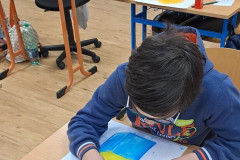 Chlapec maluje geometrické tvary křídovými barvami.