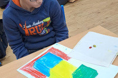 Chlapec maluje geometrické tvary křídovými barvami.